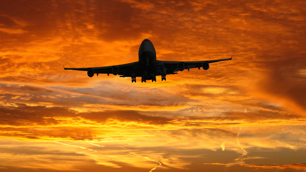 Commercial airplane flying across a glowing sunset sky during an evening flight over Europe.