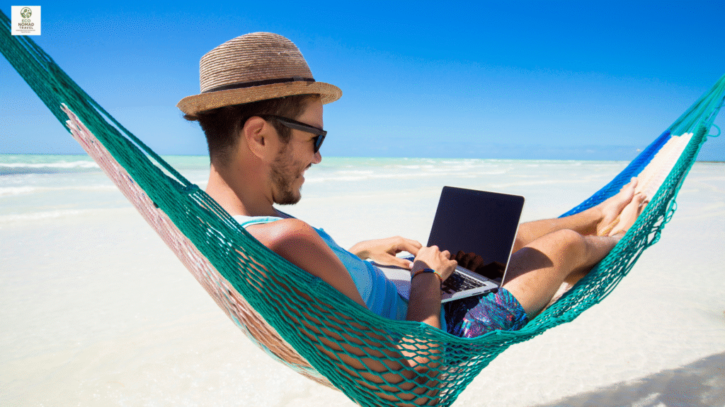 Man working remotely on a laptop while relaxing in a hammock on a tropical beach — digital nomad lifestyle 2025